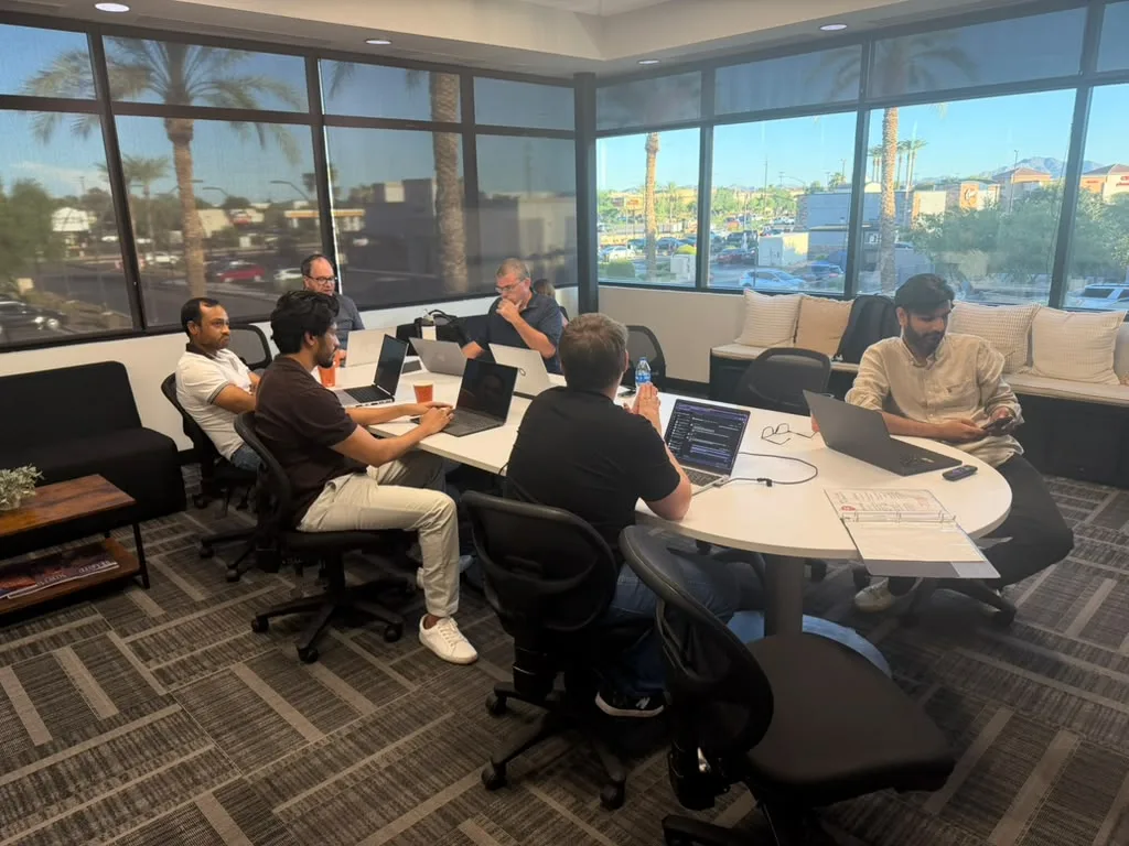 Attendees at laptops around the table before the session, with the street and palm trees through the windows.